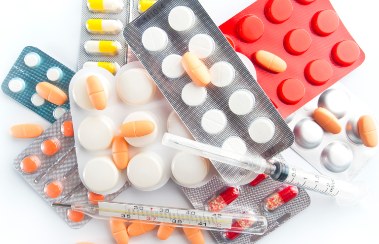 Safe Handling of Medications Assorted tablets, capsules, and a syringe scattered across a surface.