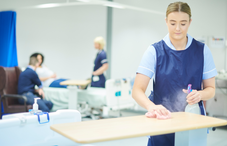 Infection Control A healthcare worker cleans a table in a hospital setting while patients are treated nearby.