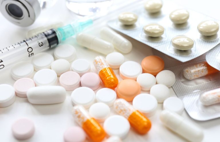 Safe Handling of Medications A variety of pills, a syringe, and a blister pack of tablets on a white surface.