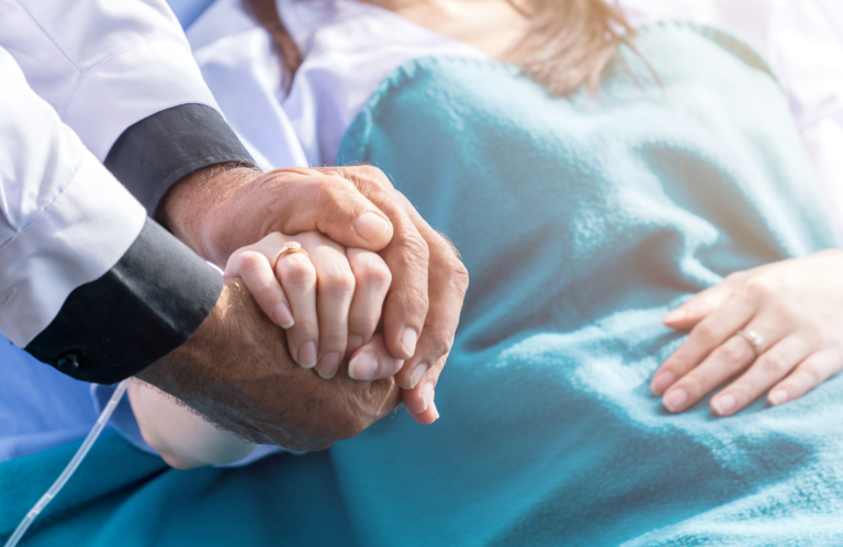 Recognising a Deteriorating Patient A doctor holds a patient's hand beside a hospital bed.