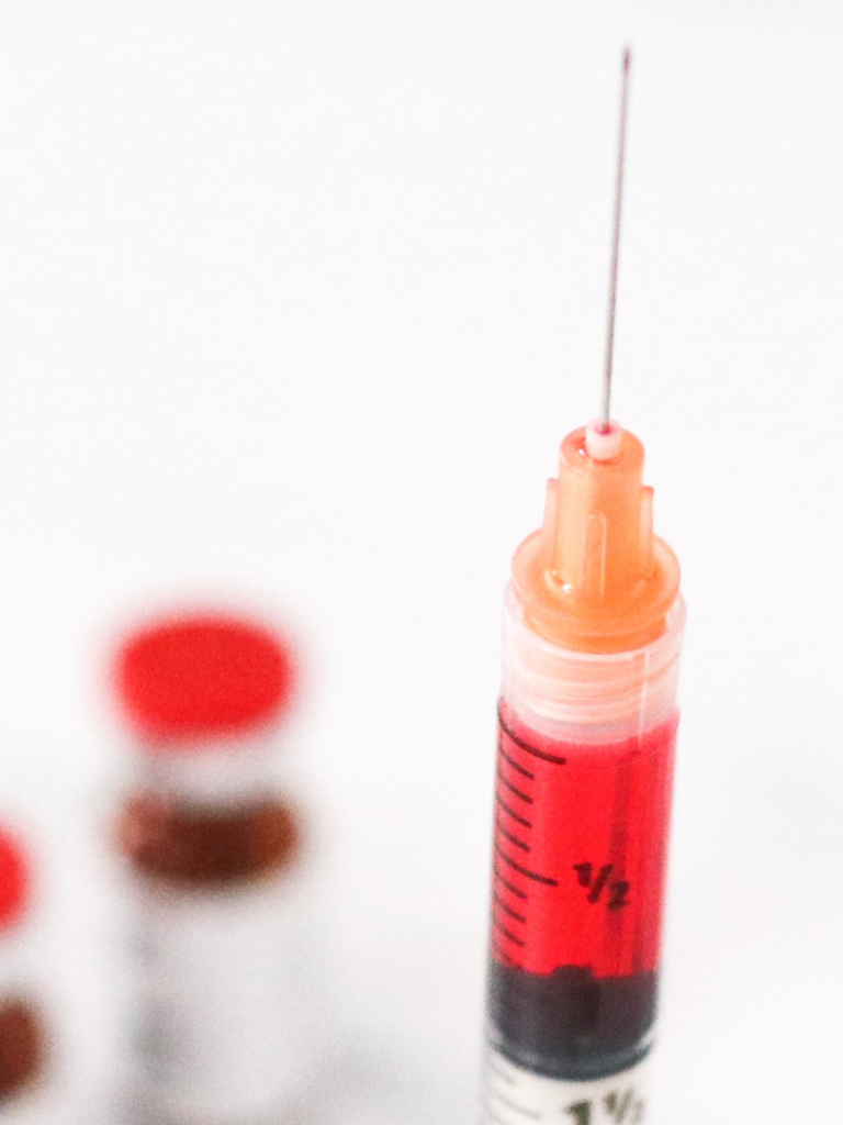 B12 Injection Syringe filled with red liquid, with vials in the background.