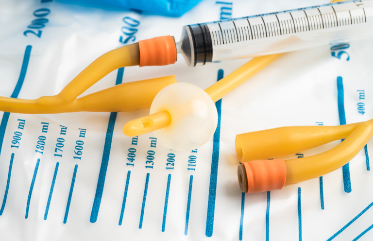 Catheter Care Image A gloved hand holding a flexible rubber catheter on a medical surface.