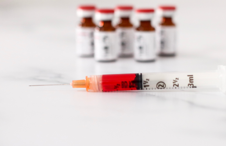B12 Injection Syringe filled with B12 next to several brown vials on a marble surface.