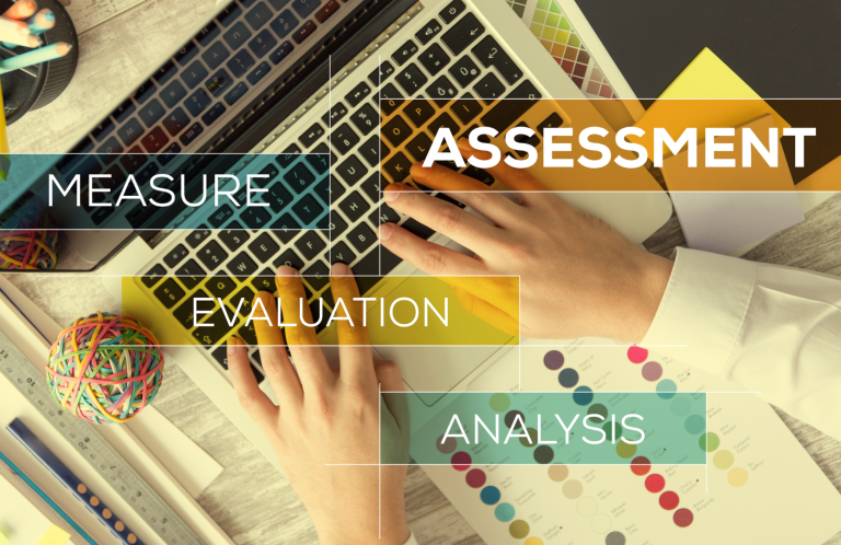 Risk Assessment Hands on a keyboard surrounded by colourful items and text labels related to analysis and assessment.