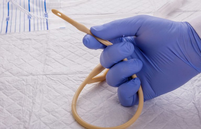 Catheter Care Image A gloved hand holding a flexible rubber catheter on a medical surface.