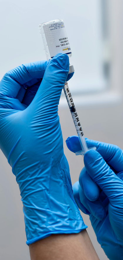 Vaccination A gloved hand holds a syringe ready for vaccination with a vial in the background.